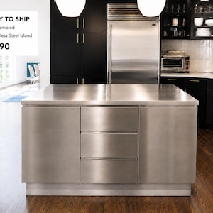 Può includere: Un'isola cucina in acciaio inossidabile con tre cassetti e un ampio piano di lavoro. L'isola è lunga 152 cm ed è completamente assemblata. La cucina presenta mobili neri e un frigorifero in acciaio inossidabile.