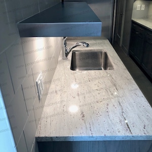 May include: A white countertop with a stainless steel sink and faucet. The countertop is made of granite with a white and gray pattern. The sink is under a stainless steel shelf.