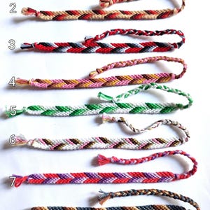 May include: Nine handmade friendship bracelets in various colors. Each bracelet is intricately woven with a chevron pattern. Colors include yellow, blue, red, black, white, green, pink, brown, and purple. The bracelets are displayed on a white surface.