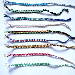 Puede incluir: Nueve pulseras de amistad coloridas con un patrón de chevron. Las pulseras están hechas con hilos de diferentes colores y están atadas con un nudo en el extremo.
