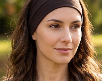 May include: A wide, dark brown fabric headband worn across the forehead. The headband is made of a smooth, solid-colored material that sits flat against the hair, providing a simple and functional accessory for securing hair away from the face.
