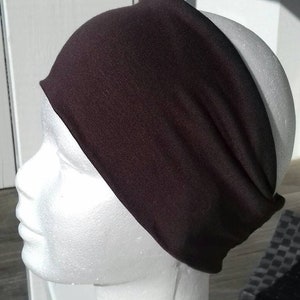 May include: A dark brown headband made of a soft, stretchy fabric. The headband is worn on a white mannequin head.