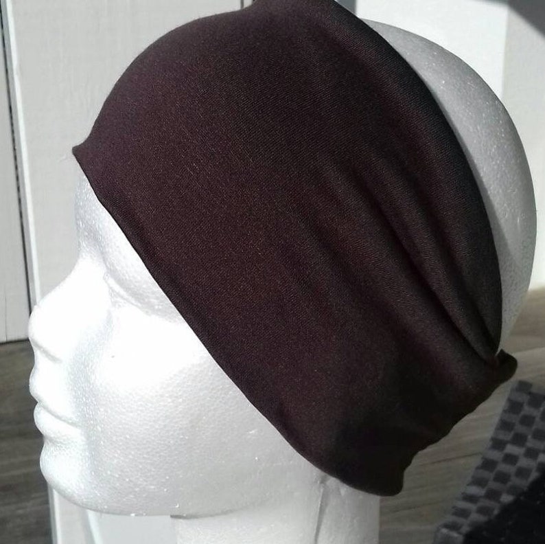 May include: A dark brown headband made of a soft, stretchy fabric. The headband is worn on a white mannequin head.