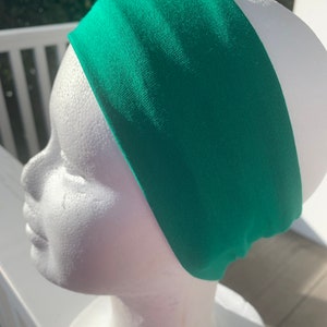 May include: A bright green headband made of a soft, stretchy fabric. The headband is shown on a white mannequin head.