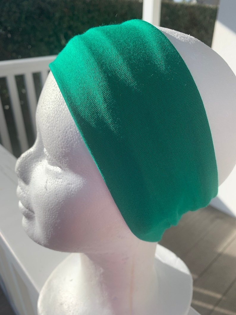 May include: A bright green headband made of a soft, stretchy fabric. The headband is shown on a white mannequin head.