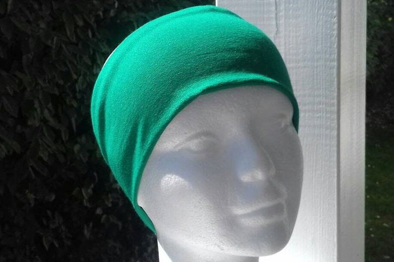 May include: A bright green headband made of soft fabric. The headband is worn on a white mannequin head.