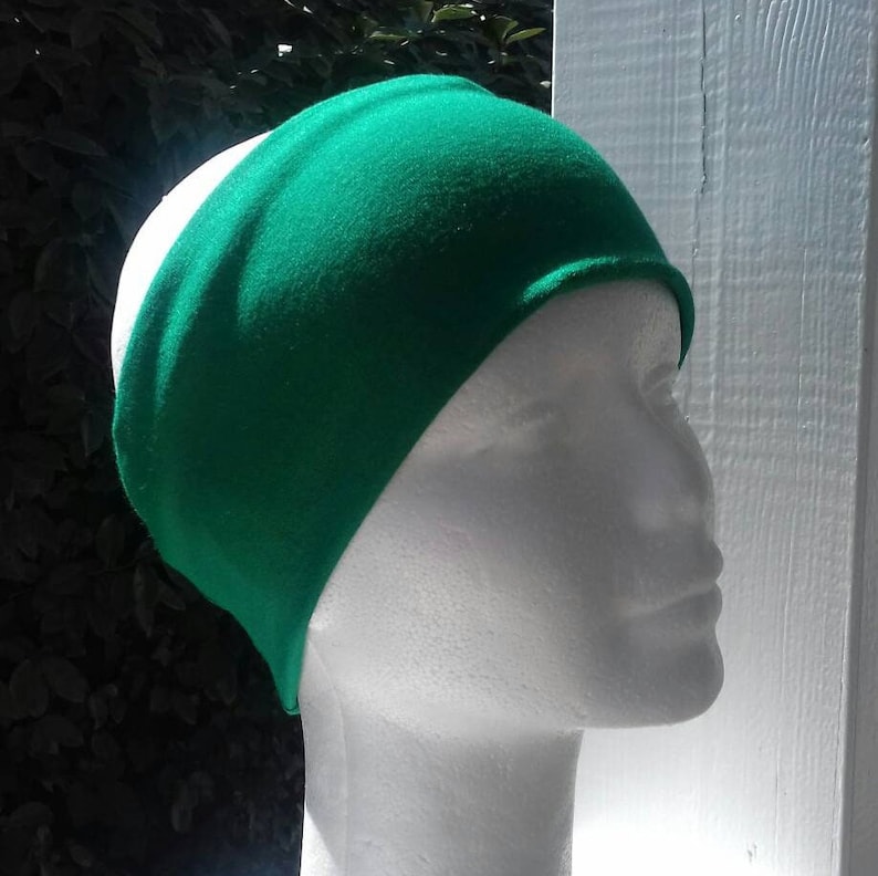 May include: A solid green headband made of soft fabric. The headband is worn on a white mannequin head.
