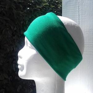 May include: A bright green headband made of soft fabric. The headband is shown on a white mannequin head.