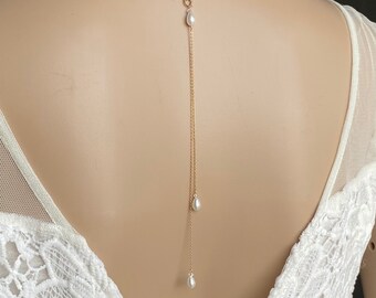 May include: A delicate gold chain with three pearl drops hangs from the back of the neck. The chain is worn by a model with a white lace dress.