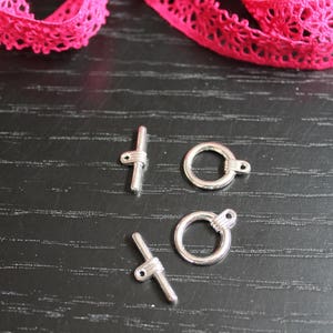 Peut inclure: Quatre fermoirs en métal argenté pour la fabrication de bijoux. Deux sont ronds avec une petite boucle sur le côté. Deux sont en forme de croix avec une petite boucle sur le dessus.