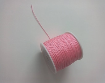 May include: A spool of pink waxed cord, a type of string used for jewelry making and crafts.