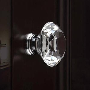 May include: A clear crystal cabinet knob with a faceted design and a silver metal base.