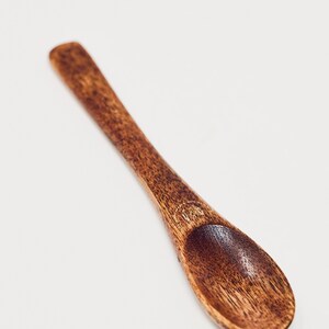 May include: A small, wooden spoon with a rounded end. The spoon is dark brown and has a smooth, polished finish.