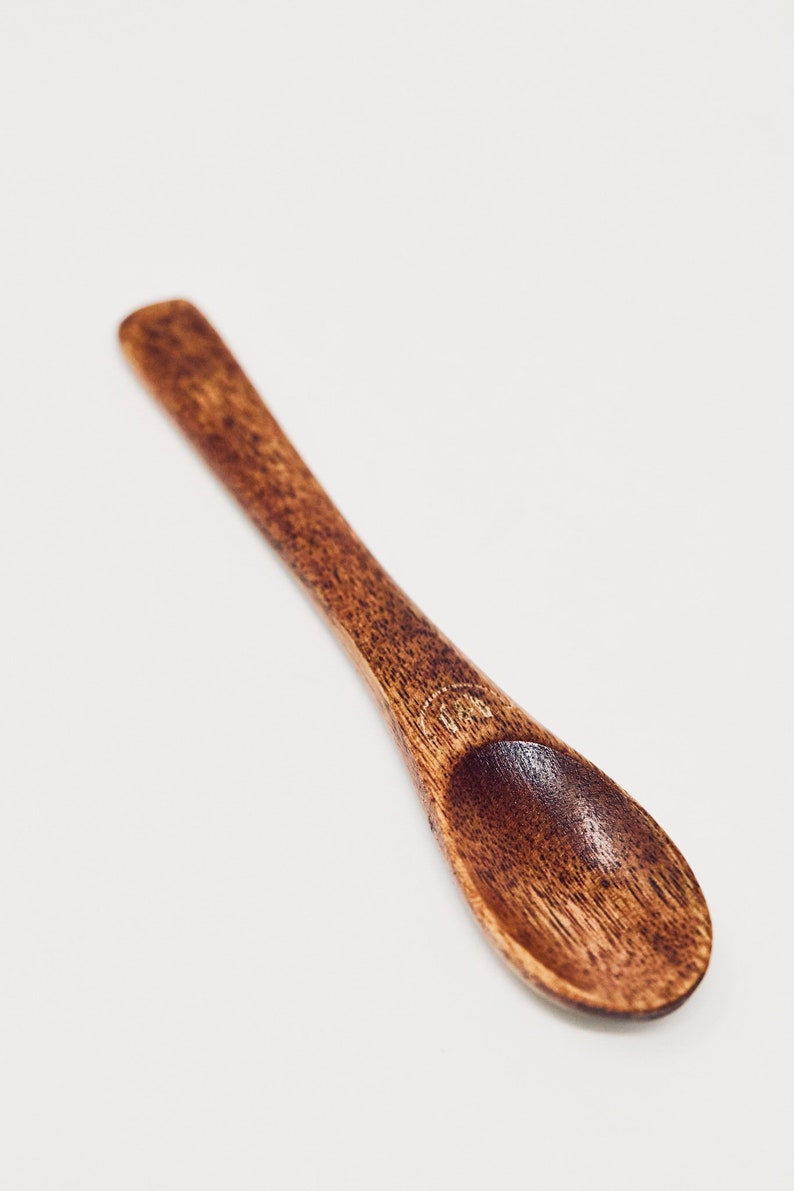 May include: A small, wooden spoon with a rounded end. The spoon is dark brown and has a smooth, polished finish.