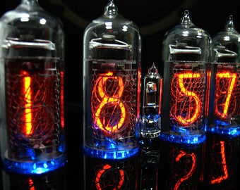May include: A close-up of four red glowing Nixie tubes displaying the time 18:57. The tubes are encased in clear glass and have a blue glow at the bottom.