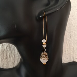 Pode incluir: Brincos de argola dourados com uma pedra branca e detalhes de contas douradas.