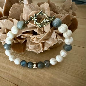 May include: A bracelet made with white and grey beads with a decorative metal clasp. The bracelet is on a brown surface.
