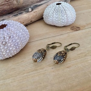 Pode incluir: Um par de brincos de bronze com contas de vidro transparente em forma de l&aacute;grima. As contas t&ecirc;m uma superf&iacute;cie texturizada e s&atilde;o adornadas com desenhos florais de bronze.
