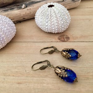 Pode incluir: Um par de brincos pendentes com uma conta de vidro azul em forma de l&aacute;grima e detalhes em lat&atilde;o antigo.