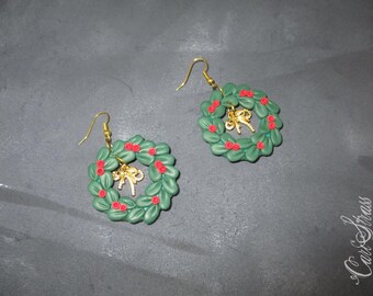 May include: A pair of green and red Christmas wreath earrings with gold accents. The wreaths are made of polymer clay and feature a small gold bow in the center.