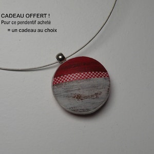Peut inclure: Un pendentif rond sur un collier en fil métallique argenté. Le pendentif présente un motif horizontal avec une section supérieure rouge, une fine bande centrale à motifs blancs et rouges, et une base texturée blanche et grise usée.