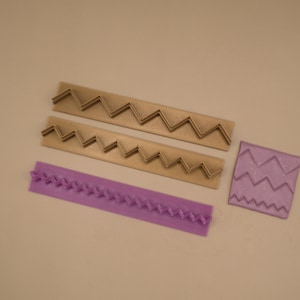 Puede incluir: Dos herramientas rectangulares de plástico color canela con un patrón de zigzag en relieve en el centro, una herramienta rectangular de plástico morado con textura trenzada en relieve y una pequeña herramienta cuadrada de plástico morado con tres líneas en zigzag.