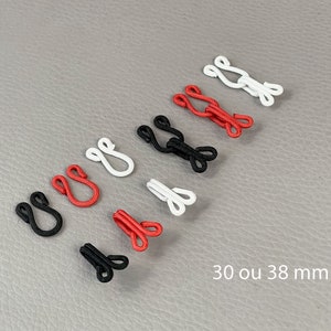 Puede incluir: Surtido de cierres de gancho y ojo en negro, rojo y blanco. La imagen muestra varios conjuntos de estos cierres, con el texto "30 ou 38 mm" que indica su tamaño. Estos cierres se utilizan para prendas de vestir.
