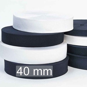 Puede incluir: Apilados rollos de cinta elástica negra y blanca, cada uno de 40 mm de ancho. La cinta elástica está enrollada firmemente, mostrando una textura acanalada. La imagen está bien iluminada, resaltando el contraste de colores.