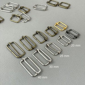 Puede incluir: Una variedad de hebillas correderas rectangulares de metal en varios acabados, incluyendo plata, oro y latón antiguo. Los tamaños varían de 20 mm a 40 mm. Adecuadas para correas de bolsos, cinturones y proyectos de manualidades.