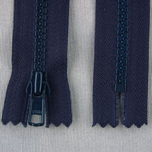 May include: Close-up of two navy blue zippers, one open and one closed. The open zipper shows the YKK brand on the pull tab. The zippers are on a textured, light beige and white striped background.