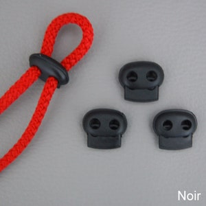 May include: Close-up of a red rope with a black cord lock and three additional black cord locks. The word "Noir" is in the bottom right corner. The cord lock is designed to secure the rope.