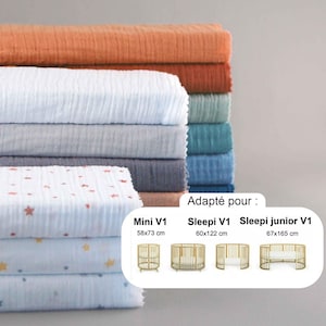 Op de afbeelding: Een stapel gevouwen babybeddengoed in diverse kleuren, waaronder oranje, wit, grijs en blauw. De onderste lagen hebben een sterrenpatroon. De afbeelding bevat de tekst: "Adapté pour : Mini V1 58x73 cm, Sleepi V1 60x122 cm, Sleepi junior V1 67x165 cm."