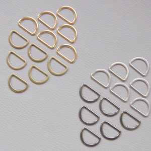 Pode incluir: Uma coleção de argolas em D em vários acabamentos metálicos, incluindo dourado, latão, prata e cinza escuro. Estas argolas em forma de semicírculo estão dispostas em grupos, mostrando as suas diferentes cores e acabamentos. Ideal para artesanato e projetos de hardware.