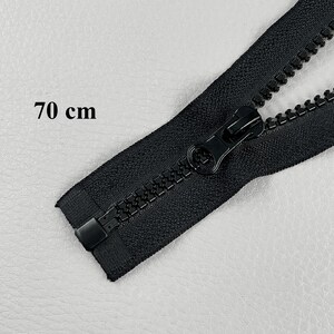 May include: A black zipper, 70 cm (27.5 inches) long, with a matching pull tab. The zipper teeth are interlocked, and the slider is in the closed position. The zipper is made of a durable material.