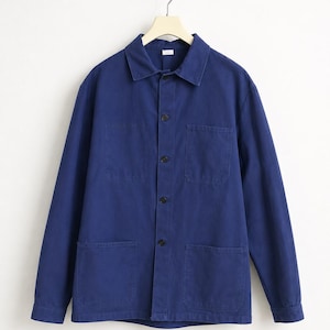 Peut inclure: Veste de travail bleu marine avec une fermeture boutonnée, deux poches de poitrine et deux poches inférieures. La veste est suspendue sur un fond blanc. La veste est en tissu résistant.