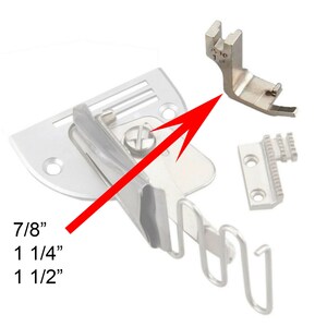Può includere: Un set di accessori argentati per macchina da cucire. L'immagine mostra un piedino premistoffa, un attacco per rilegatura e un trasporto. Il piedino premistoffa è contrassegnato con le misure: 7/8", 1 1/4", e 1 1/2".
