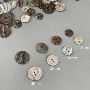 Puede incluir: Surtido de botones redondos en varios tamaños y colores. Algunos botones son blancos nacarados, mientras que otros son marrones con aspecto texturizado. Tamaños: 15 mm, 18 mm, 20 mm y 25 mm.