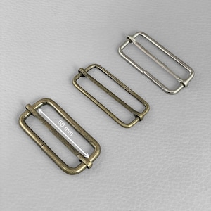 Puede incluir: Tres deslizadores rectangulares de metal en acabados de latón antiguo y plata. El deslizador de latón antiguo mide 50 mm de largo. Estos deslizadores se utilizan para ajustar correas en bolsos, cinturones y otros accesorios.