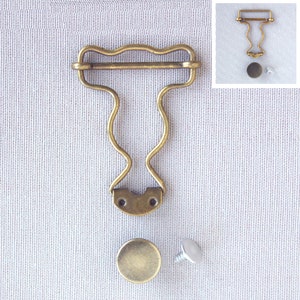 Könnte beinhalten: Antikes Messing-Bilderrahmen-Hardware-Set. Das Set enthält einen dekorativen Bilderrahmenaufhänger, eine runde Kappe und eine Schraube. Der Aufhänger hat ein wellenförmiges Top-Design und geschwungene Seiten. Die Hardware ist für Bilderrahmen konzipiert.