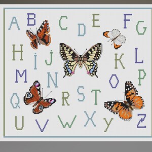 May include: Cross-stitch design featuring the alphabet with colorful butterflies. The letters are in shades of blue, green, and purple. The butterflies have orange, brown, yellow, and white wings. The design is framed with a light blue border.