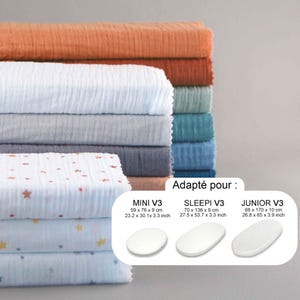 Pode incluir: Uma pilha de tecido dobrado e texturizado em várias cores, incluindo laranja, branco, cinza e azul. Algumas peças têm um padrão de estrelas. A imagem inclui o texto "Adapté pour" e medidas para MINI V3, SLEEPI V3 e JUNIOR V3.