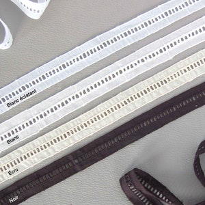 Puede incluir: Primer plano de cuatro cintas de diferentes colores con un diseño recortado. Los colores son blanco, blanquecino y negro. El texto en las cintas dice "Blanc éclatant", "Blanc", "Écru" y "Noir".