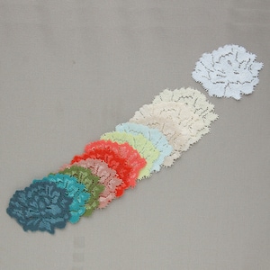 Peut inclure: Une collection de napperons en dentelle colorés dans diverses teintes, dont le turquoise, le vert, le rouge et la crème. Les napperons sont disposés en diagonale, avec un isolé en haut. Le motif floral délicat est visible sur chaque pièce.