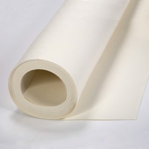 Puede incluir: Un rollo de papel blanquecino, parcialmente desenrollado, revelando las capas internas. El papel parece liso y de grosor medio, adecuado para diversos usos artísticos o artesanales. El rollo se encuentra sobre un fondo blanco liso.