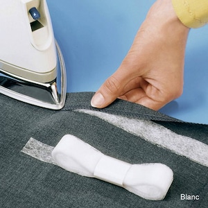 Peut inclure: Un fer à repasser blanc est utilisé pour presser un tissu gris foncé. Un matériau blanc en forme de ruban est placé sur le tissu. Le mot "Blanc" est visible en bas à droite. Le fond est bleu clair uni.