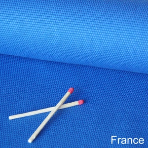 Pode incluir: Close-up de um tecido azul vibrante com uma trama texturizada. Dois fósforos de madeira com pontas vermelhas estão cruzados sobre o tecido. A palavra "France" está impressa em branco no canto inferior direito.