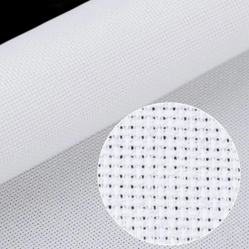 May include: Close-up of a roll of white Aida cloth, a fabric used for cross-stitch and other needlecrafts. The image shows the fabric's grid-like structure, with a magnified view of the weave in a circular inset.