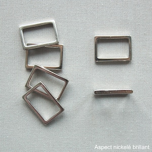 Pode incluir: Fivelas retangulares de metal prateado. Várias fivelas estão espalhadas sobre uma superfície cinza clara, com uma posicionada de lado. O texto "Aspect nickelé brillant" é visível no canto inferior direito.