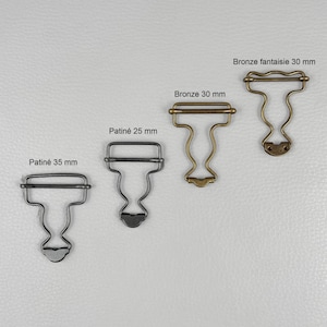 Peut inclure: Quatre boucles métalliques en finitions bronze et patinées, présentées sur fond neutre. Les boucles varient en taille, avec des mesures de 25 mm, 30 mm, 30 mm et 35 mm. Elles ont une forme décorative en T.