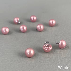 Pode incluir: Uma coleção de botões rosa, semelhantes a pérolas, com hastes de metal. Os botões são redondos e têm um acabamento brilhante. Alguns botões têm uma argola para costurar. A palavra "Pétale" é visível no canto inferior direito.